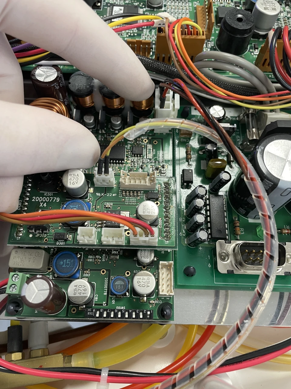 A gloved hand inspecting an electronic circuit board during equipment servicing.