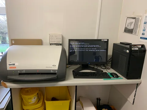 Computed radiography reader beside a monitor, keyboard and workstation computer.